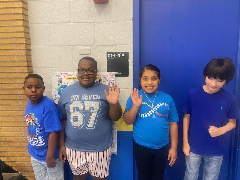 Four children stand together, facing the camera. They are in front of a blue door with a sign.