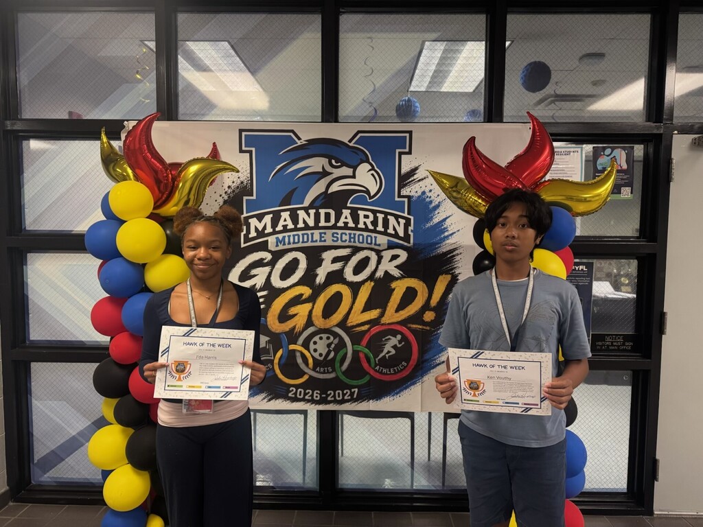 Two individuals stand with certificates in front of a banner with balloons, reading "MANDARIN GO FOR GOLD!"