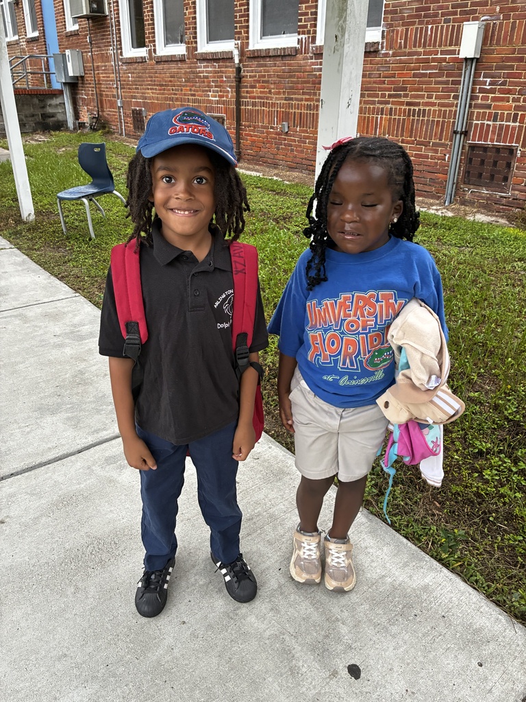 Two children stand on a sidewalk. One wears a backpack, and the other has a stuffed toy.