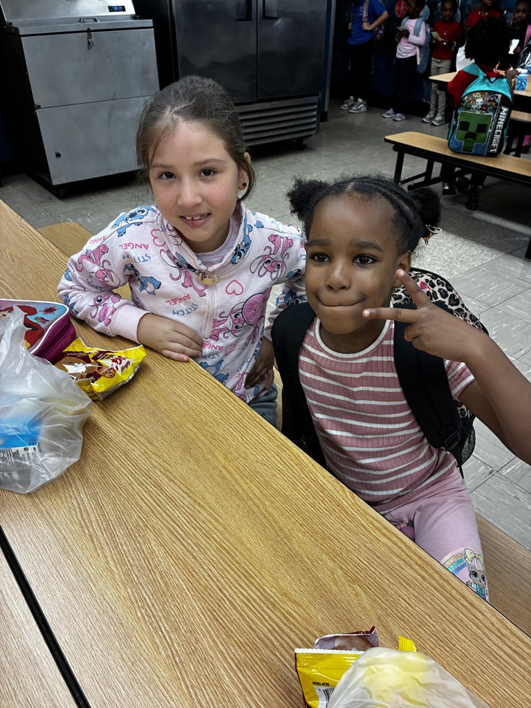 Two children, one in pink and the other in striped shirt, sit at a cafeteria table.