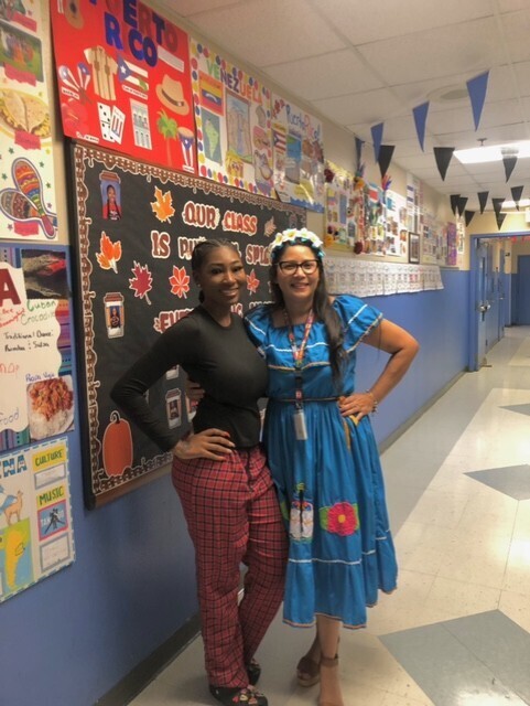 Ms. Flanders at Ms. Ingrid Carias pose for a photo in front of Ms. Flanders' hallway display for Hispanic Heritage Month. 
