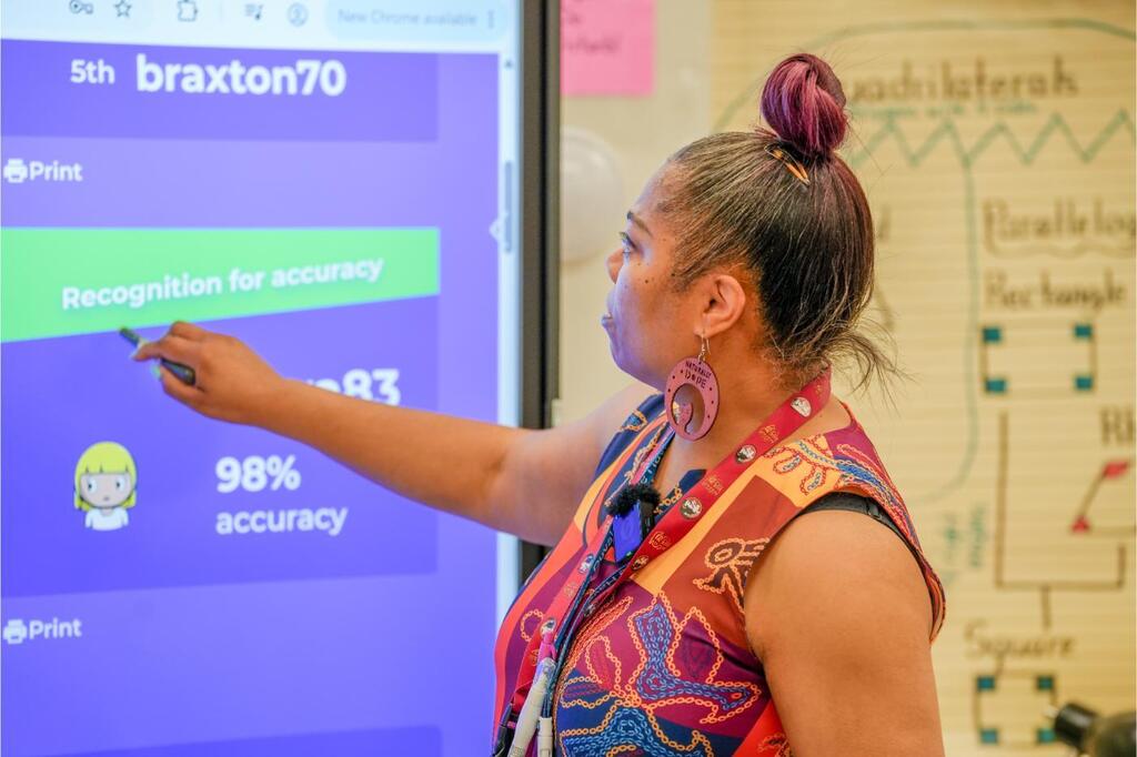 A person writes on a screen with a marker. The screen shows text and numbers. A colorful dress and hair tie are visible.