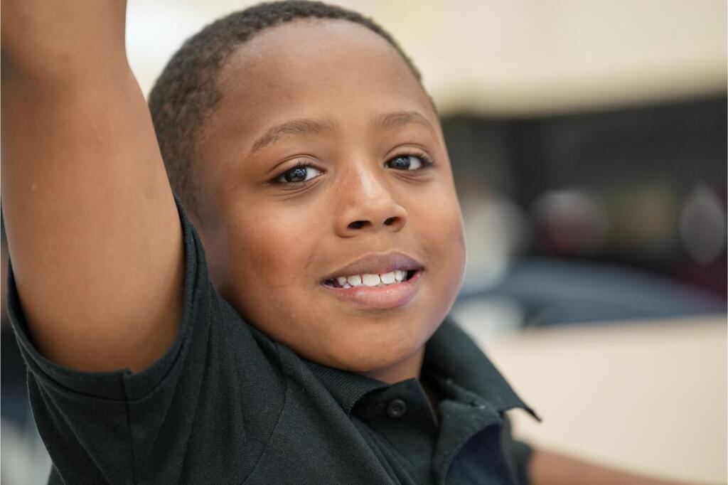 A child, with one arm raised, smiles and appears to be posing for a picture.