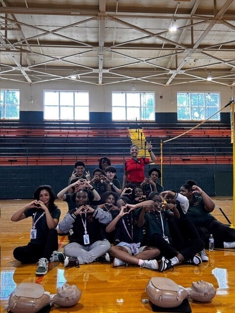 A group of people sit on a basketball court posing for a photo. Some wear IDs.