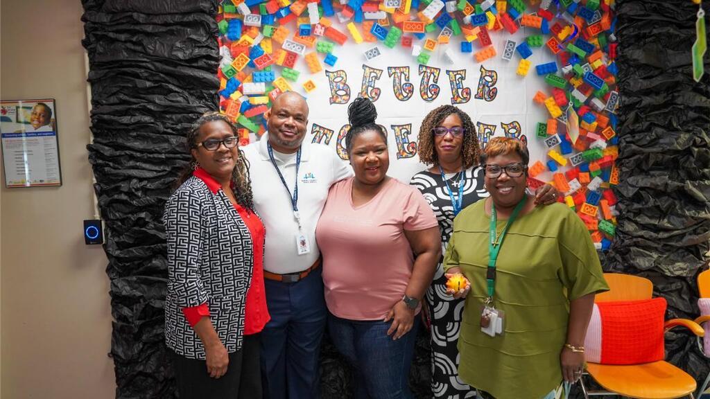 Five people standing together in front of a colorful, confetti-like backdrop with the word "BUBBEB".