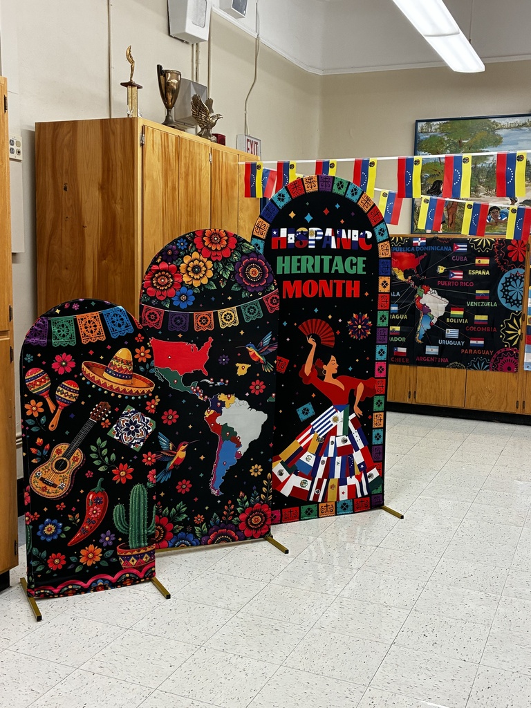 A room with displays of Latino culture. Colorful banners with a woman dancing and a guitar. White floor, wooden cabinet.