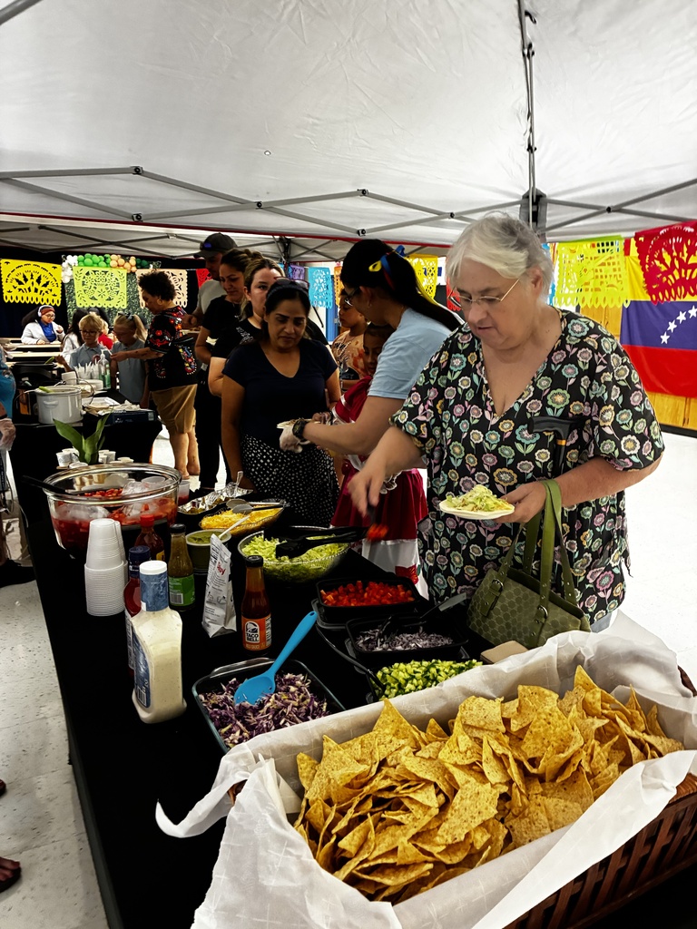 An outdoor food buffet under a tent. An older woman is serving food to a line of people.