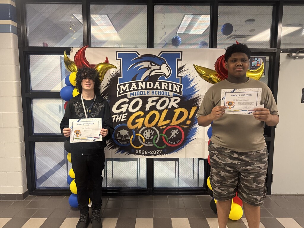Two students stand in front of a banner reading "Go for the Gold!" holding certificates.
