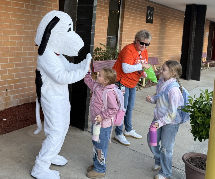 A mascot hands a cup to a child as two other children stand nearby. A woman wearing sunglasses stands behind the children.