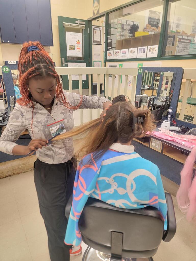 A young person sits in a salon chair while another person cuts their hair.