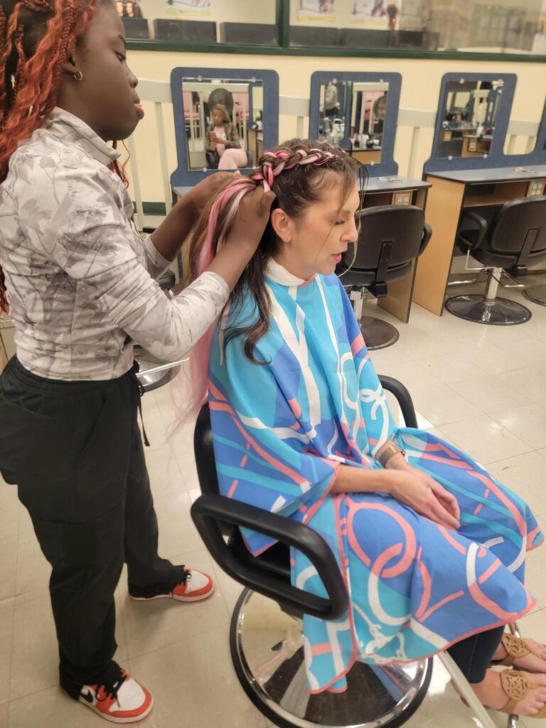A woman getting a haircut by a person in a salon, with mirrors and chairs behind them.