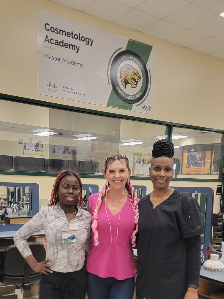 Three women in a room with salon chairs and a banner that reads "Cosmetology Academy Master Academy".