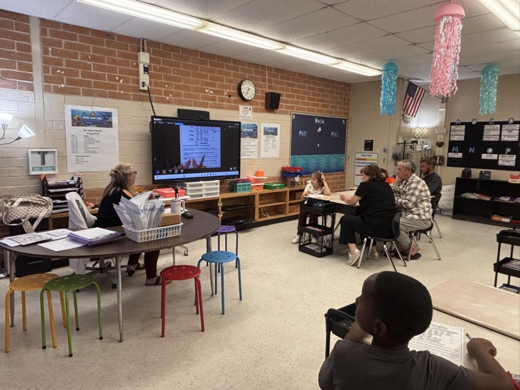 A classroom with brick walls and various desks and chairs; several people sit at tables working.