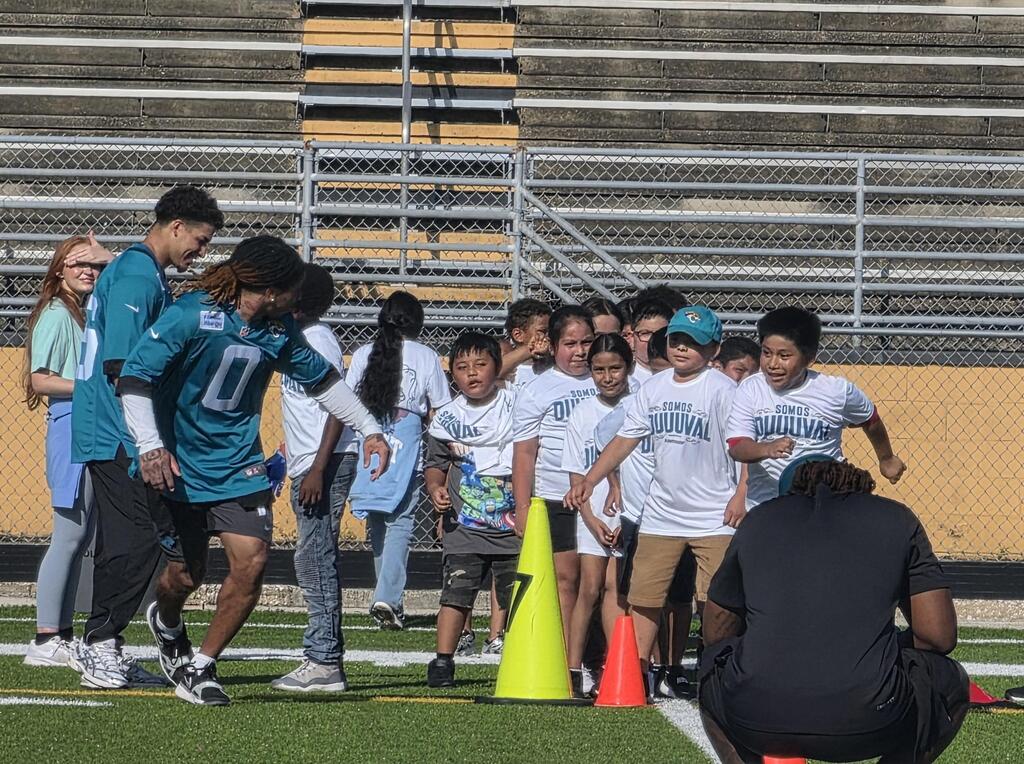 A group of students race on the football field with a member of the Jacksonville Jaguars team.