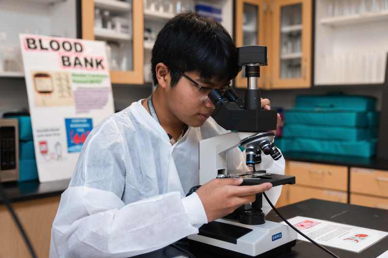 Student in classroom uses a microscope to study an object.