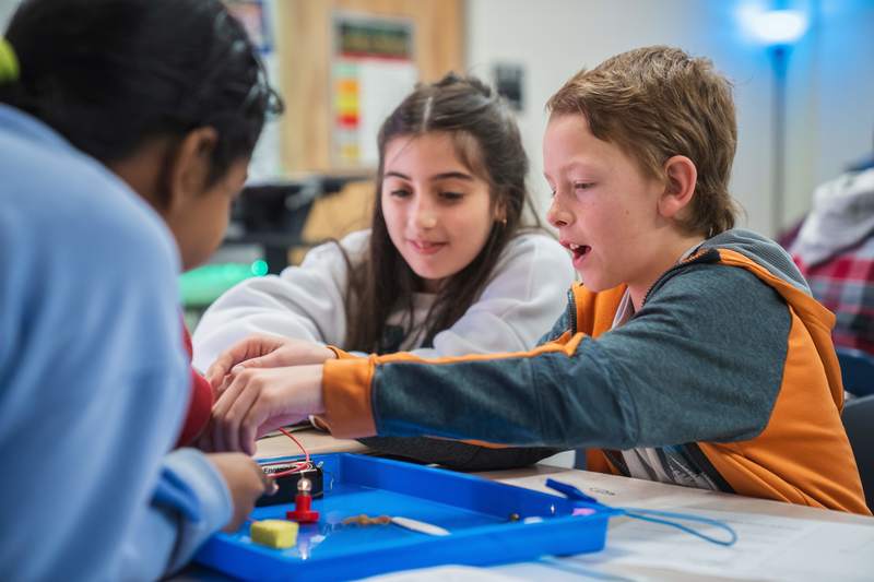 Three elementary students work together at a table on a science project