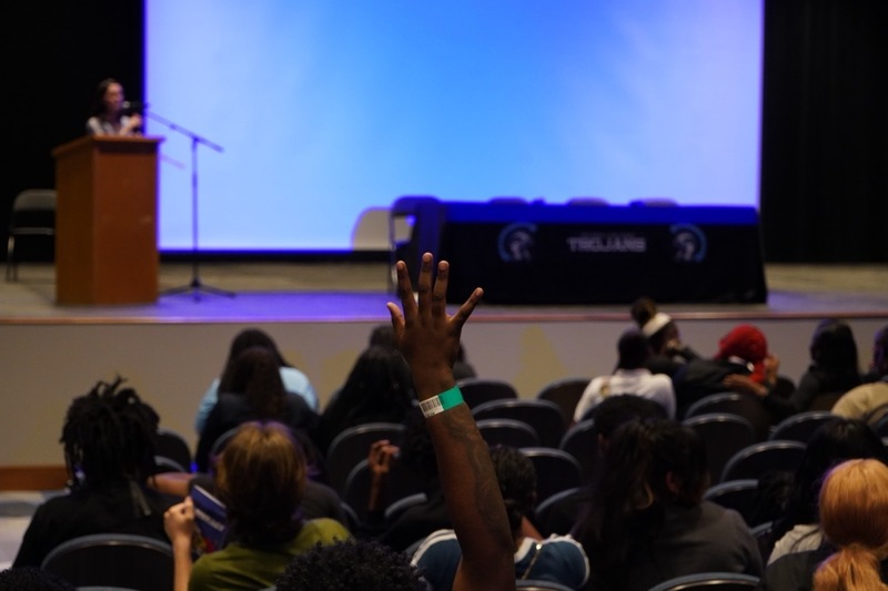 A student raises their hand while attending a question and answer session