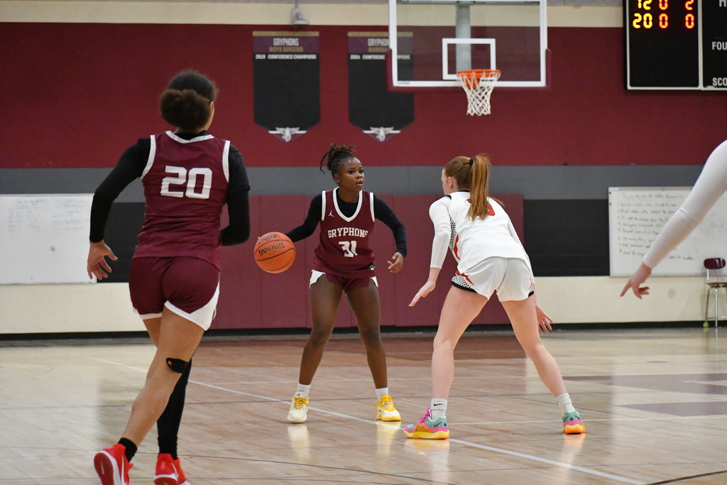 Three varsity girls playing basketball, two in a burgundy uniform and one in a white uniform