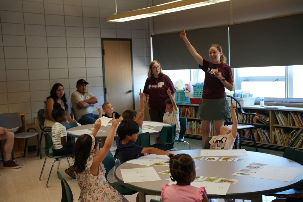 kindergarteners at tables with hands up