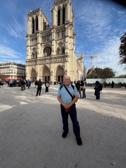 Mr. Roberson stands in front of the Notre-Dame cathedral, with a large clock tower and gothic architecture.