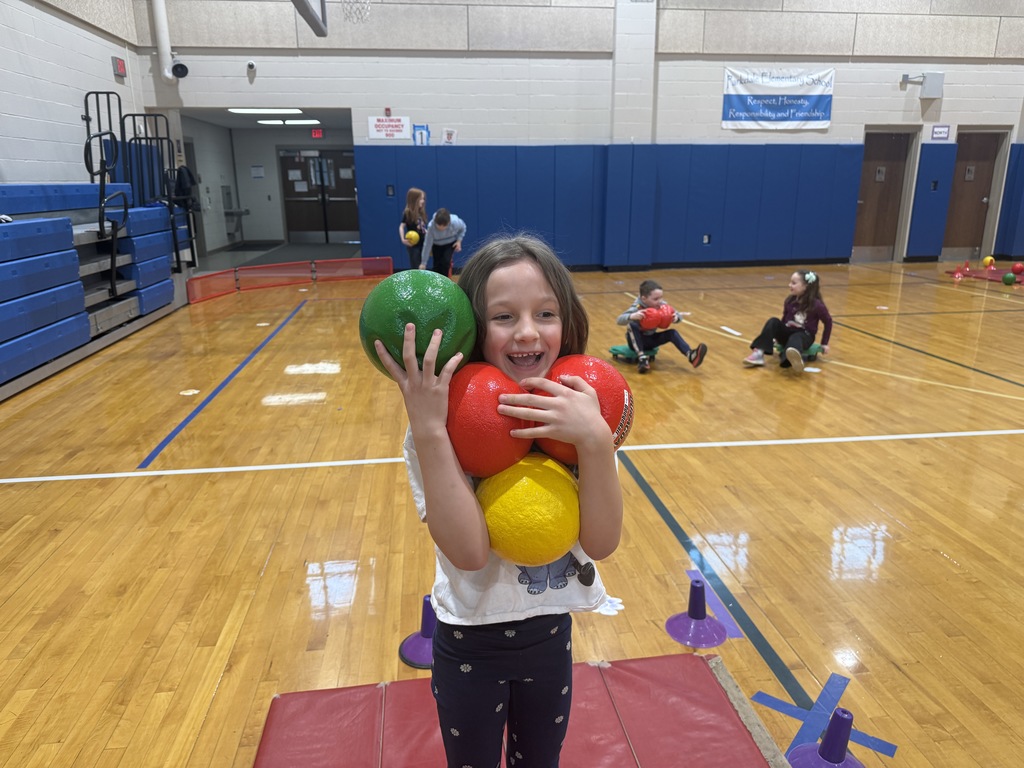 student holding colorful foam balls standing on a matt while other students roll around on scooters