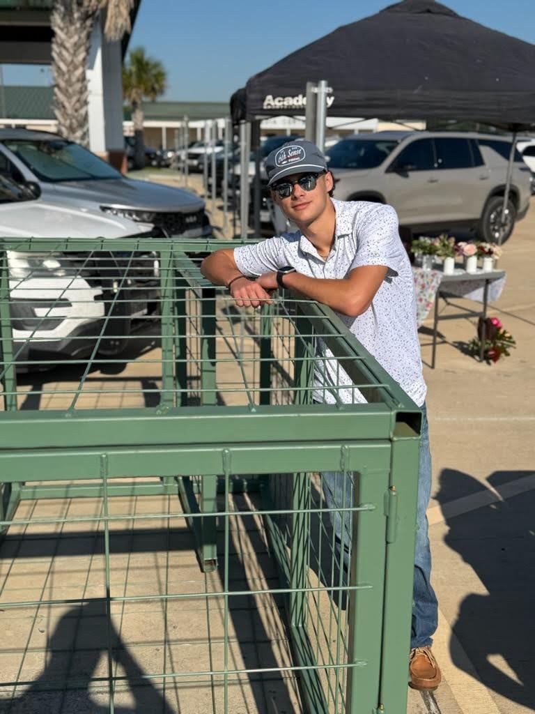 A man leans on a metal railing in a parking lot. Behind him are several cars parked.