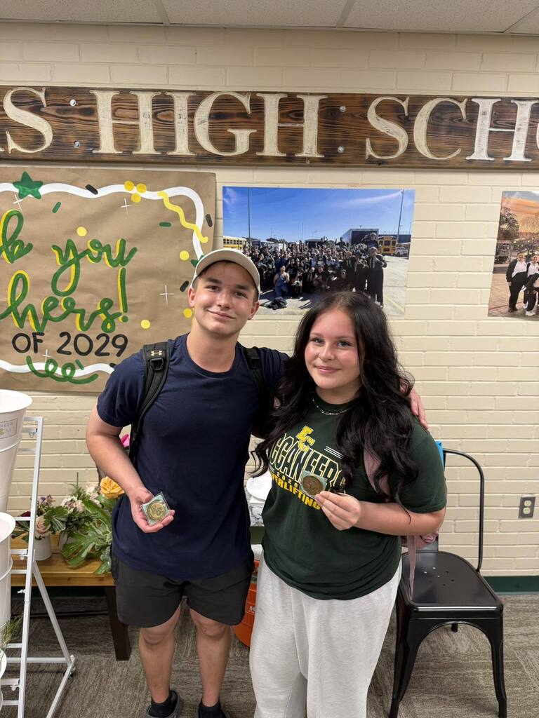 Two people stand inside a room with a banner for the school's class of 2029.