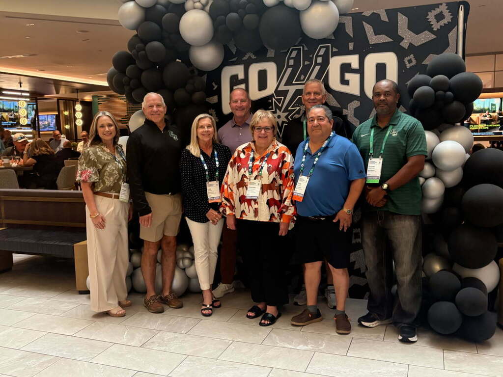 Group of adults wearing name tags standing in front of a large balloon display that says "GO GO".