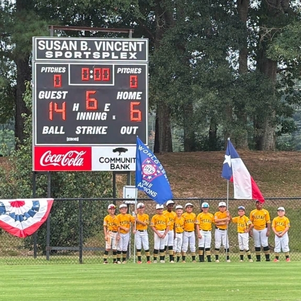 Scoreboard displays zero for both teams. Eleven children in white uniforms stand on a baseball field.