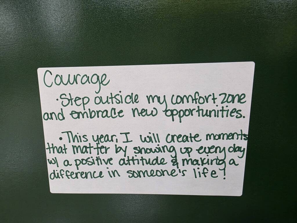 White paper on a dark surface with handwritten text in black: "Courage: Step outside my comfort zone and embrace new opportunities."