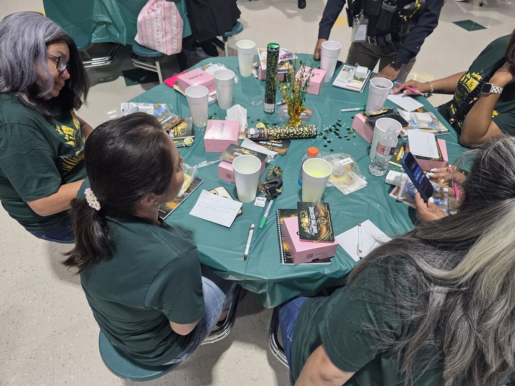 A group of women sit around a table with items on it, including cups, papers, and a cellphone.