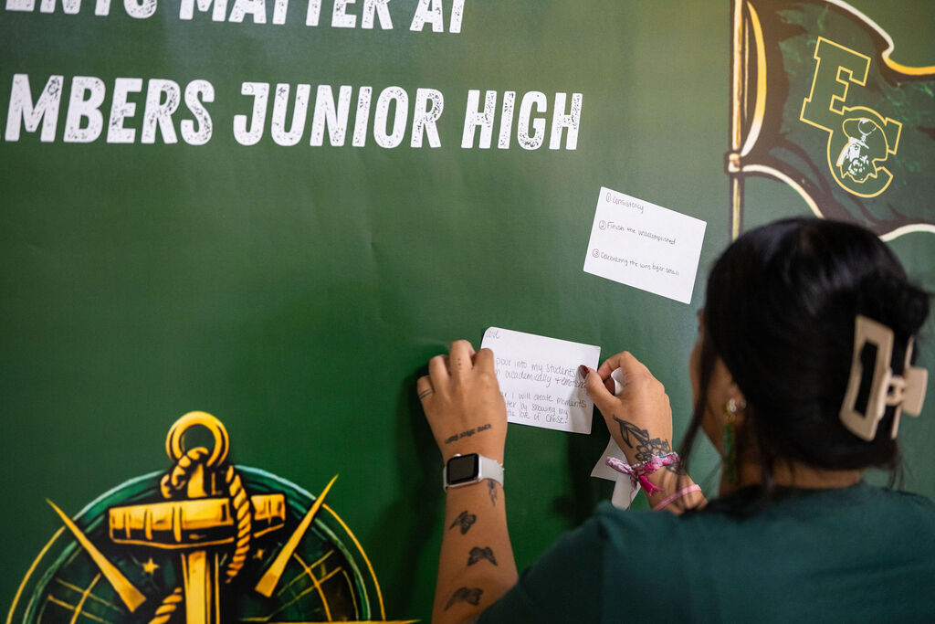 Person pinning paper on a bulletin board. Text on the board reads "Members Junior High". Logos include a shield and an anchor.