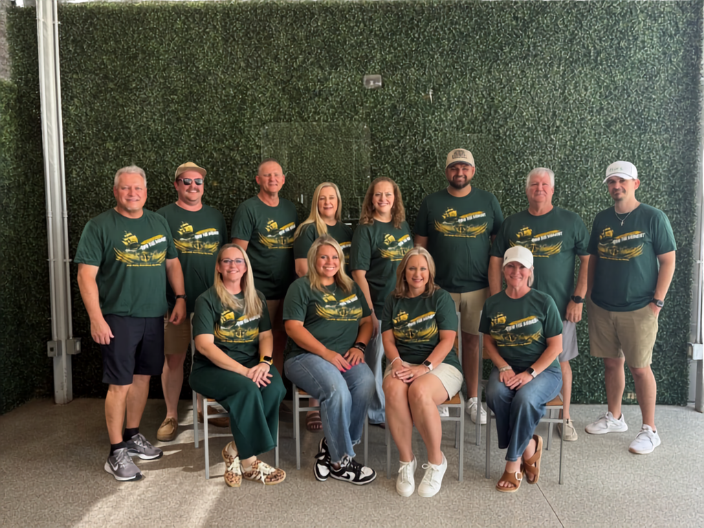 A group of people in green shirts pose for a photo in front of a green wall.