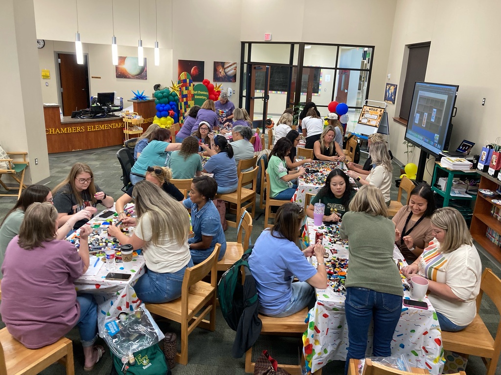 A group of people gathered around tables in a room, working on Legos. Some wear casual clothing.