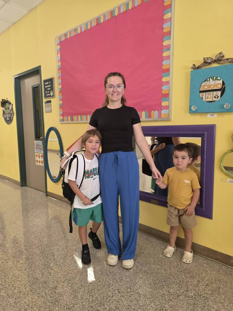 A woman with two children standing in a brightly lit hallway. They are holding hands.