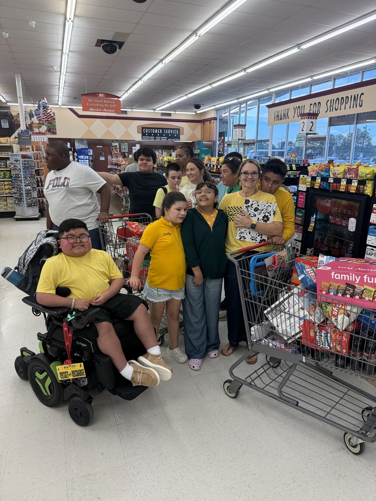 Several people stand in a supermarket, some wearing yellow shirts, with one in a wheelchair.