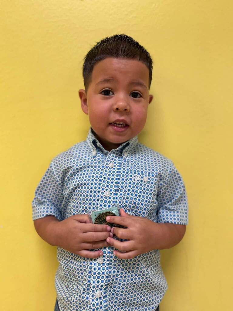 Young boy in a blue shirt with a white dot pattern, holding money. Background is yellow.
