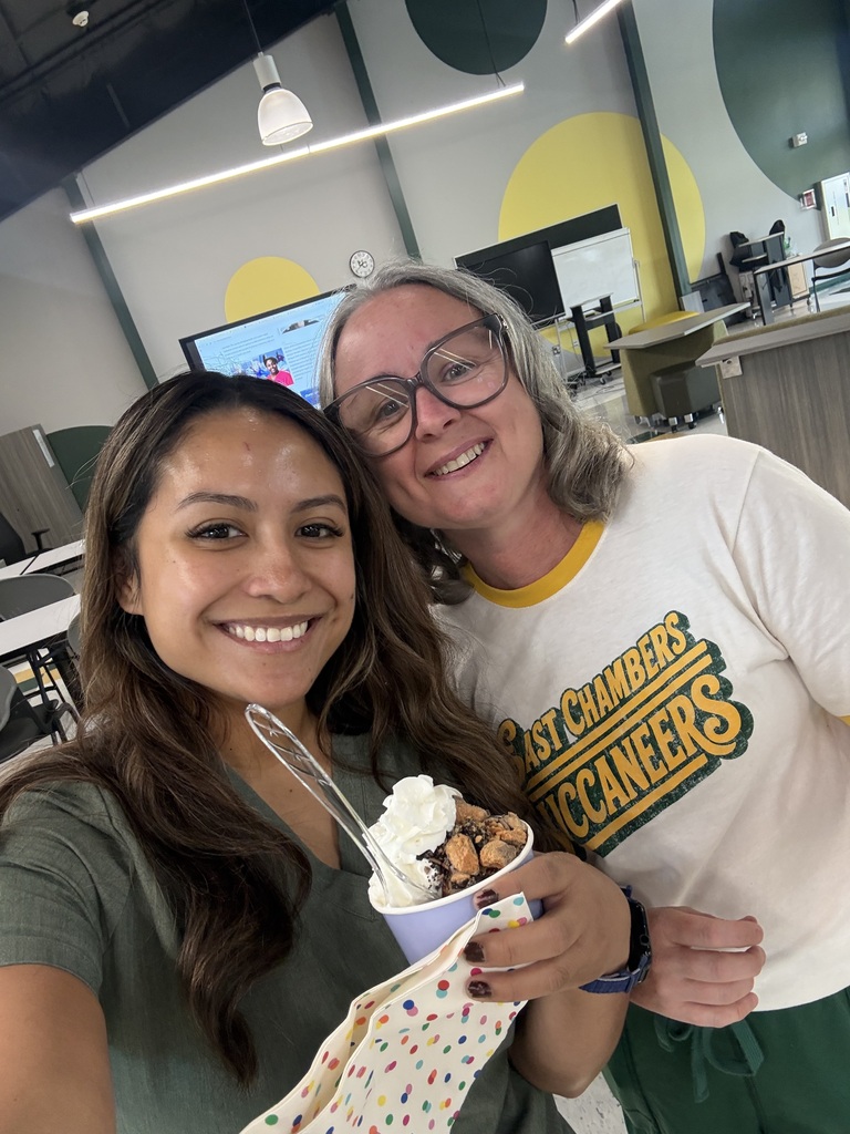 Two people posing for a photo; one holds a cone of ice cream and sprinkles.