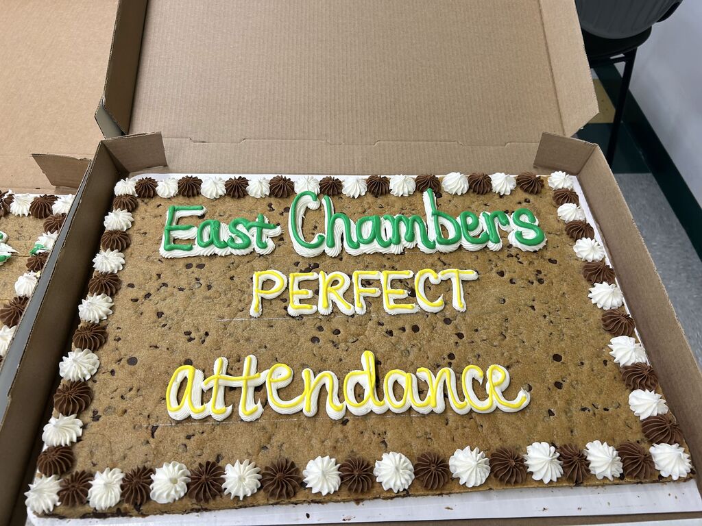 A large chocolate chip cookie cake in a box. It reads "East Chambers PERFECT attendance" with frosting decorations.