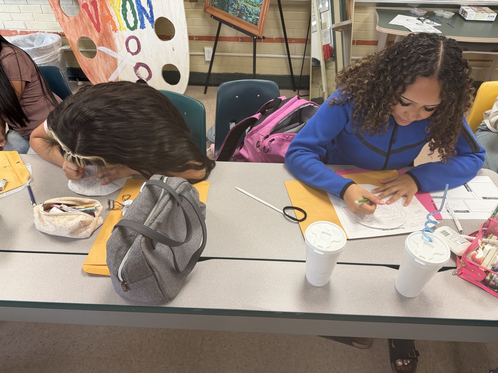 Two individuals in a classroom setting, engaged in art activities. One uses scissors on a paper, the other draws.