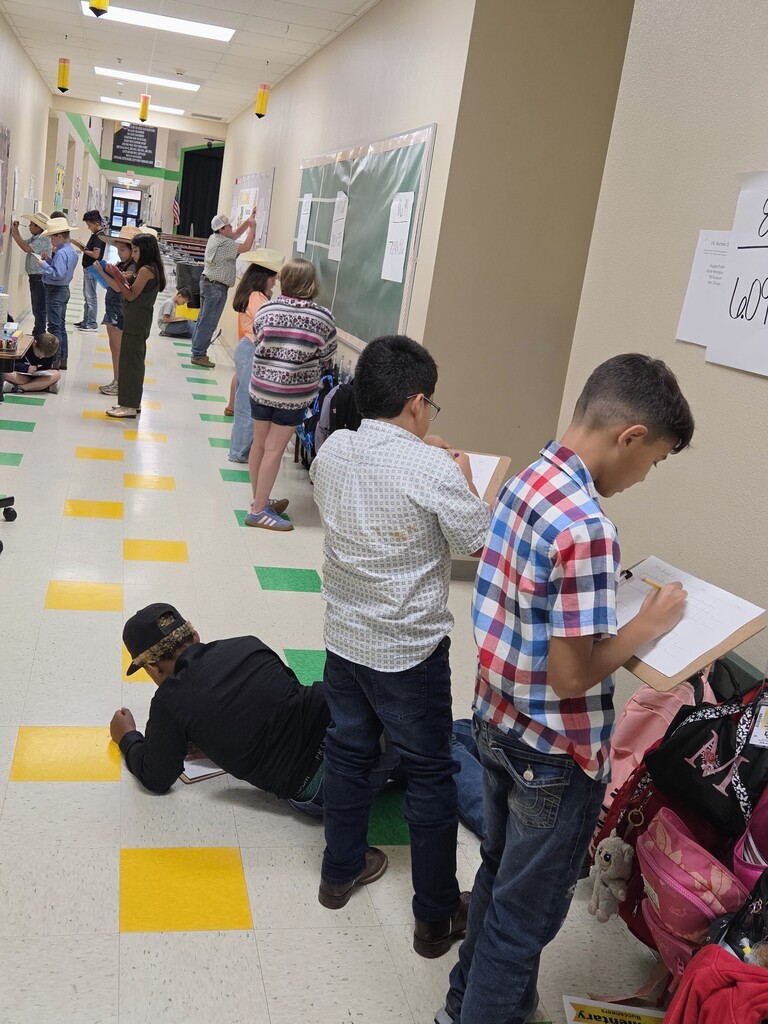 A hallway with students participating in an activity. Some lie on the floor, others stand. Yellow floor markers and white boards.