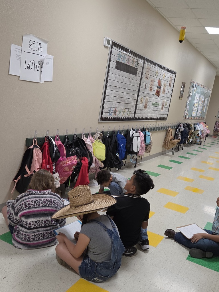 People sit on a floor around a hallway, wearing hats and shoes. Some wear bracelets. One holds a notebook.