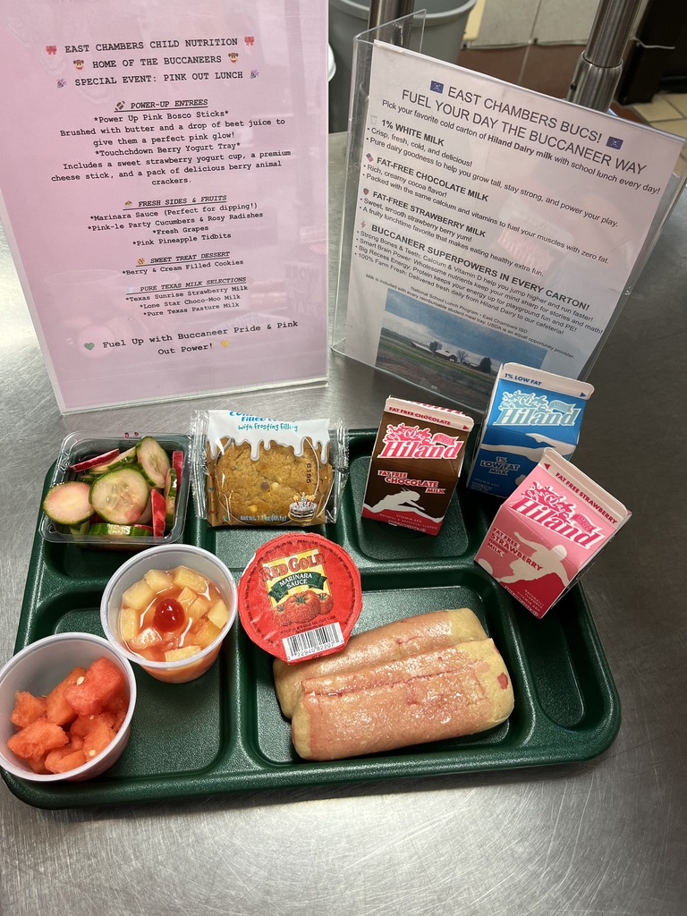 Green tray with food: fruit salad, vegetables, a sandwich, a yogurt container, and a carton of milk. Behind is a pink sign.