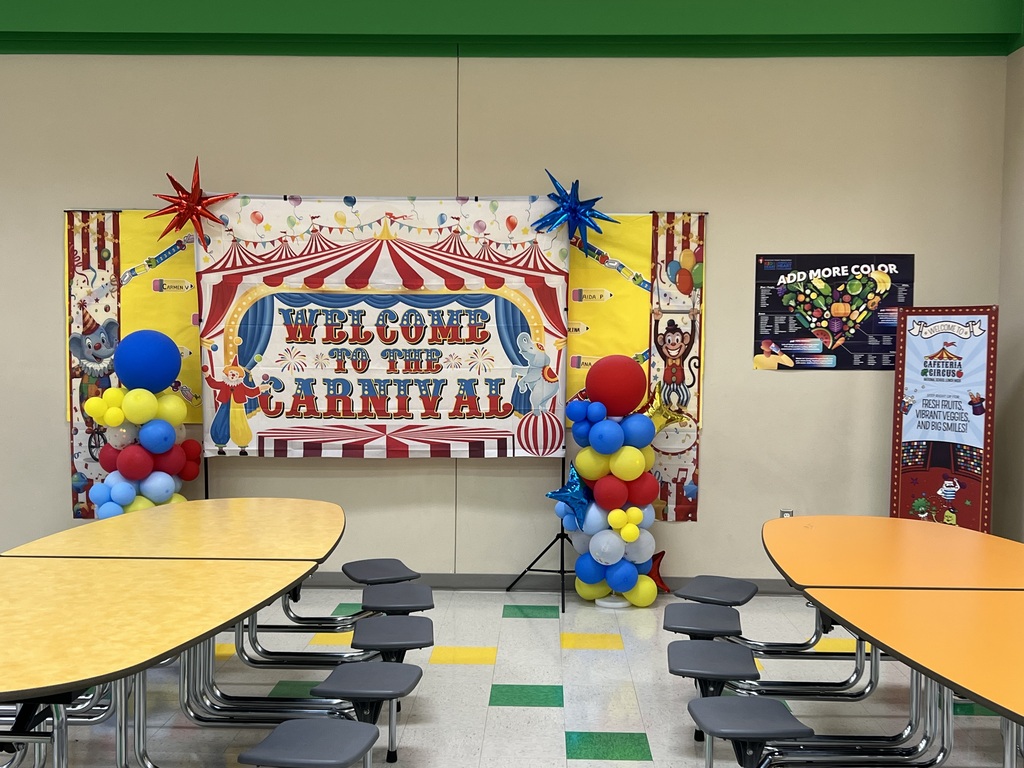 A room with tables and chairs. A colorful banner with balloons reads "Welcome to the Carnival".