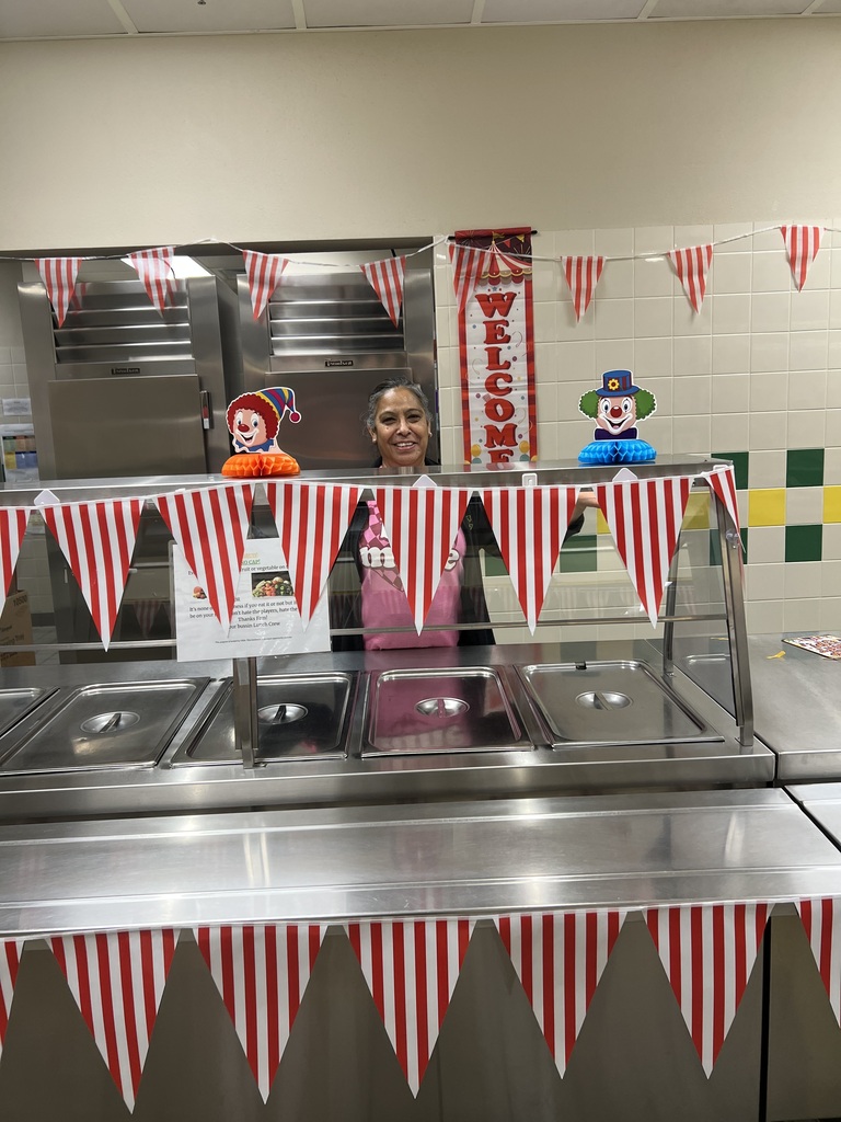 A person stands behind a counter, decorated with red and white bunting and two clown figures.