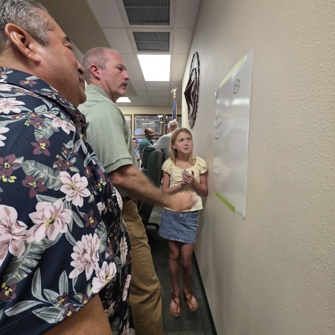 Three people inside a building, two adults holding a child, all looking up at the ceiling with an overhead light.