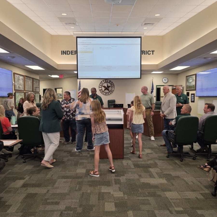 People in a room with monitors, a projector screen, and a large desk. Some stand, others walk, and a child dances.