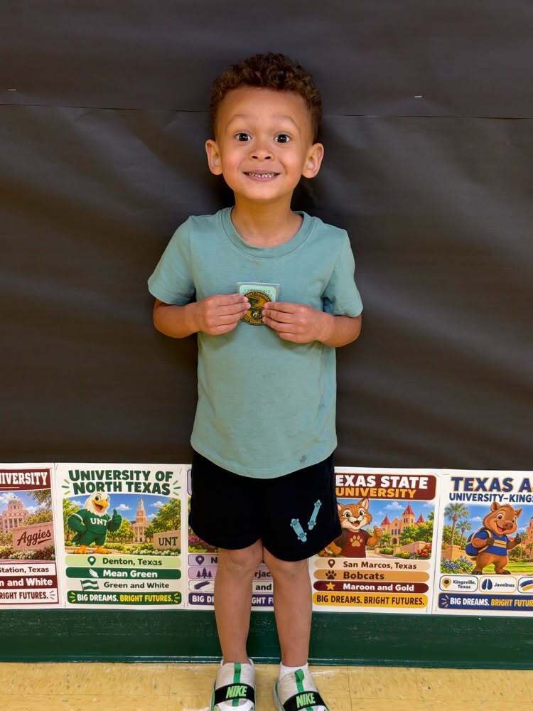 A boy, holding a medal, stands in front of a wall with educational posters from universities.