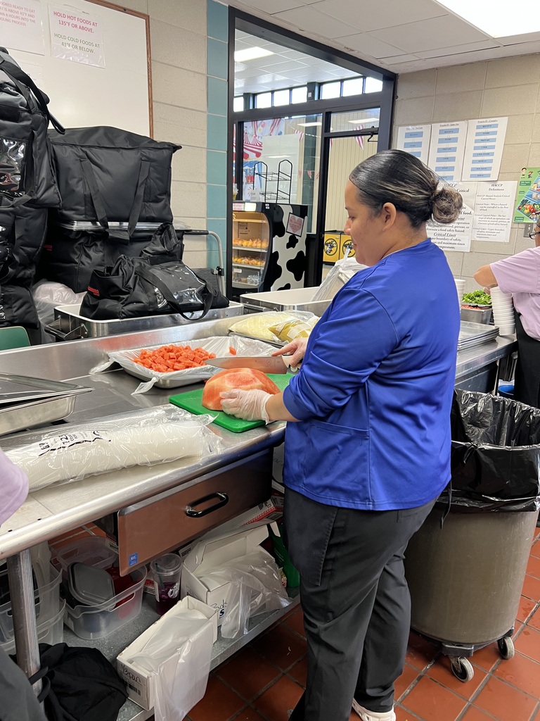 A woman in a blue shirt and gray pants is preparing food in a kitchen.