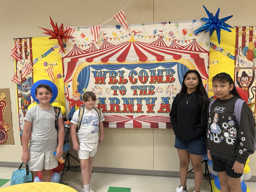 Four children stand under a banner reading "Welcome to the Carnival" in a room with balloons.